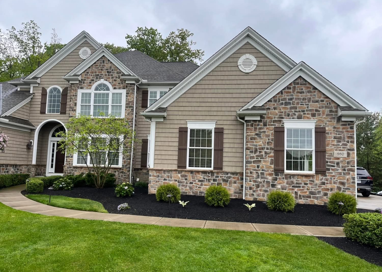 Tan stone home with freshly mulched landscape beds and decorative plantings in Auburn, Ohio